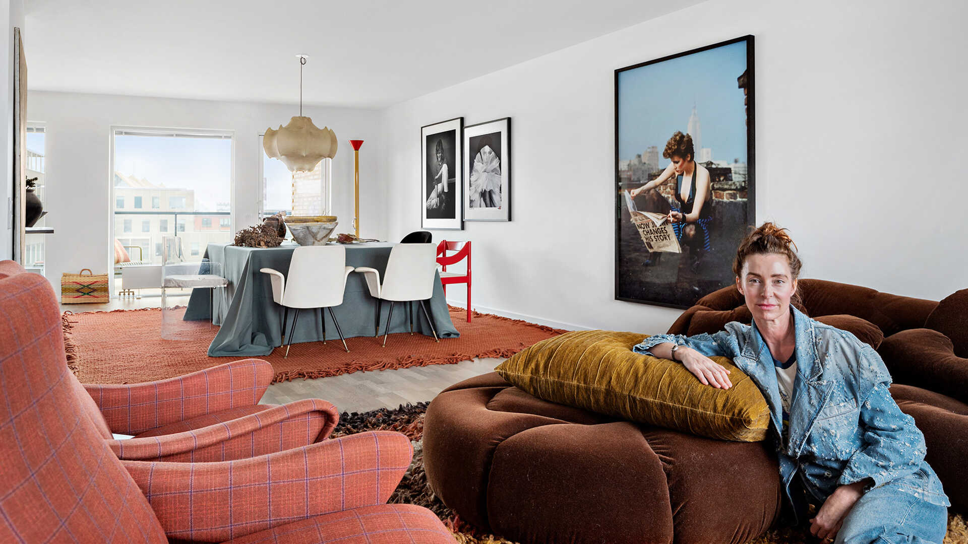 Kvinna sitter i en modern vardagsrumsinredning med designmöbler, fotografier på väggen och ett dukat bord i bakgrunden