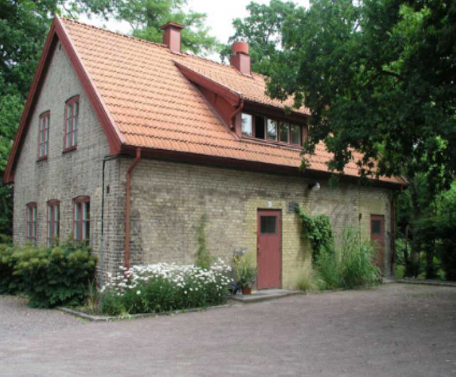 Gammalt tegelhus med röda dörrar och fönsterkarmar, omgiven av grönska och blommor