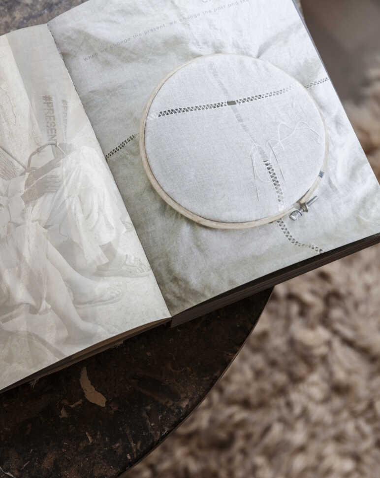 Öppen bok med ett broderibåge och tyg placerat på en marmorbord