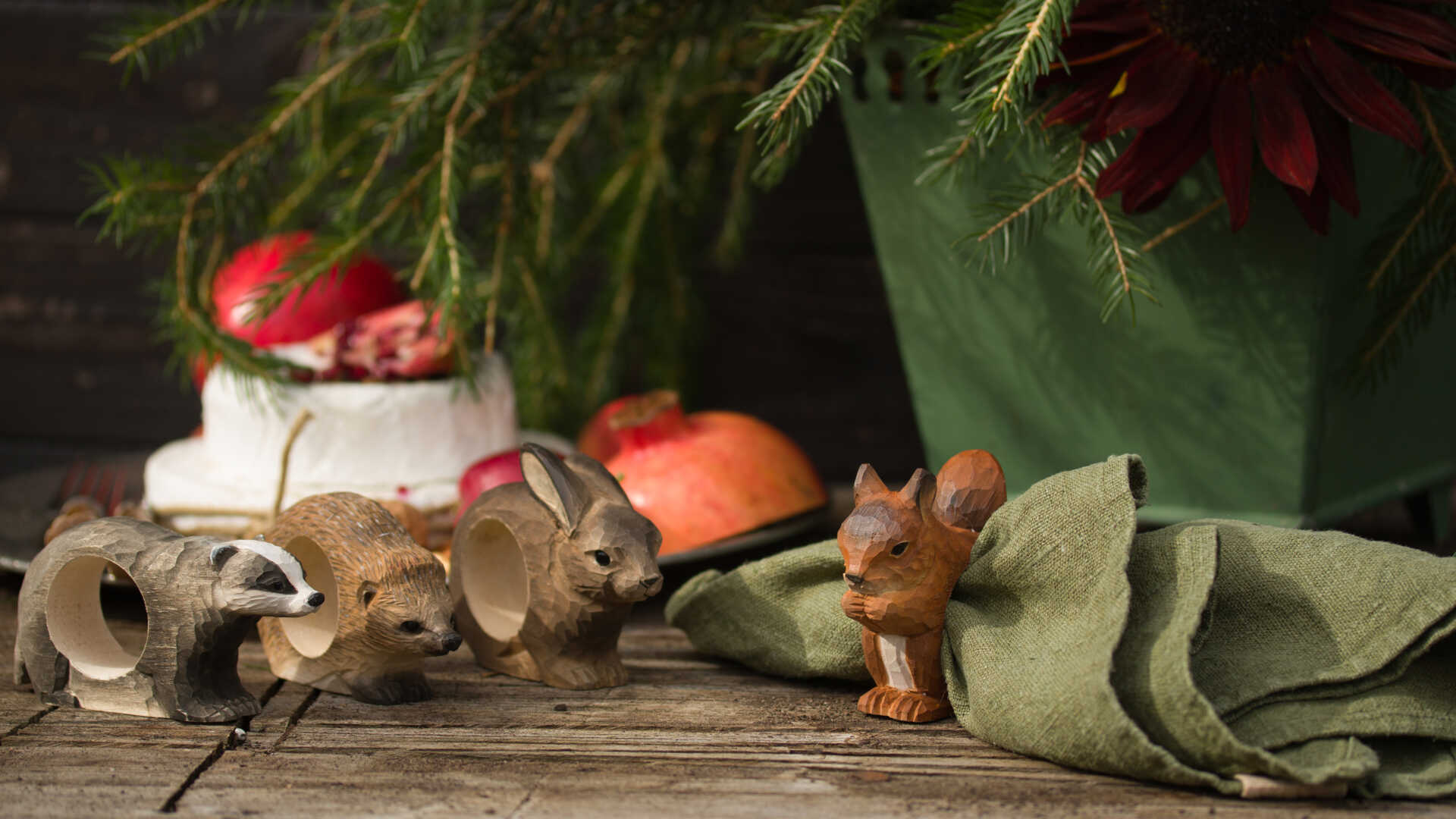 Träfigurer av djur och en grön servett på ett träbord med äpplen och gröna växter i bakgrunden