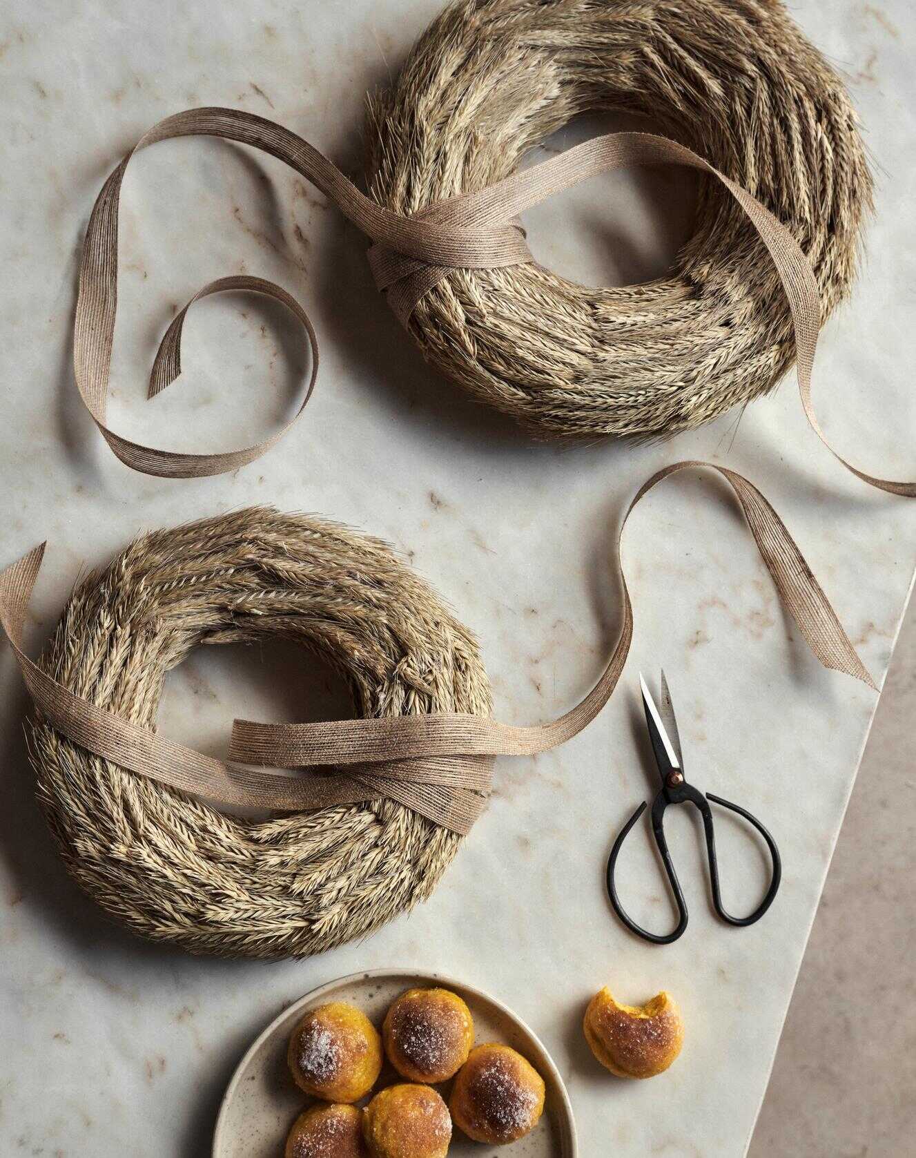 Torkade kransar av vete med band på en marmorbänk bredvid en sax och en tallrik saffransbullar