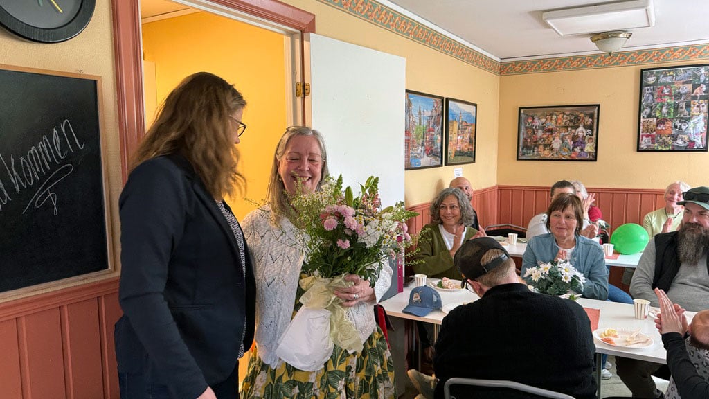 Kvinna får blombukett under en sammankomst i ett rum med flera personer som sitter runt bord
