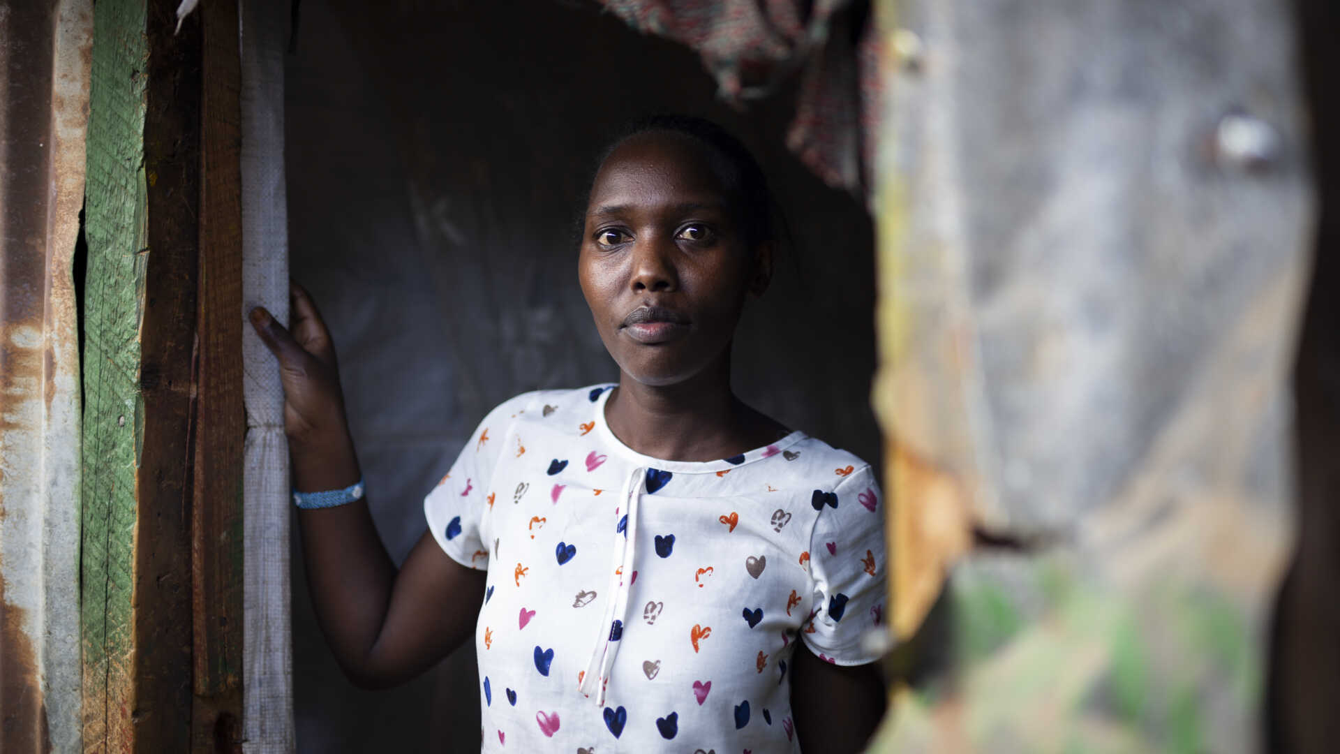 Kvinna i en vit tröja med hjärtmönster står i en dörröppning av ett enkelt hus