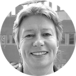 Porträtt av en leende kvinna med kort hår framför en byggnad, i svartvitt