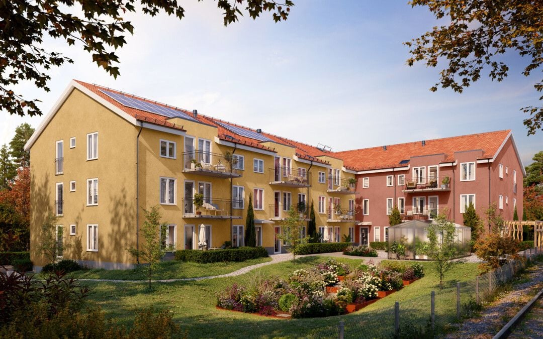 Flerfamiljshus med gul och röd fasad, balkonger och solpaneler på taket, omgivna av en grön trädgård under en klar blå himmel