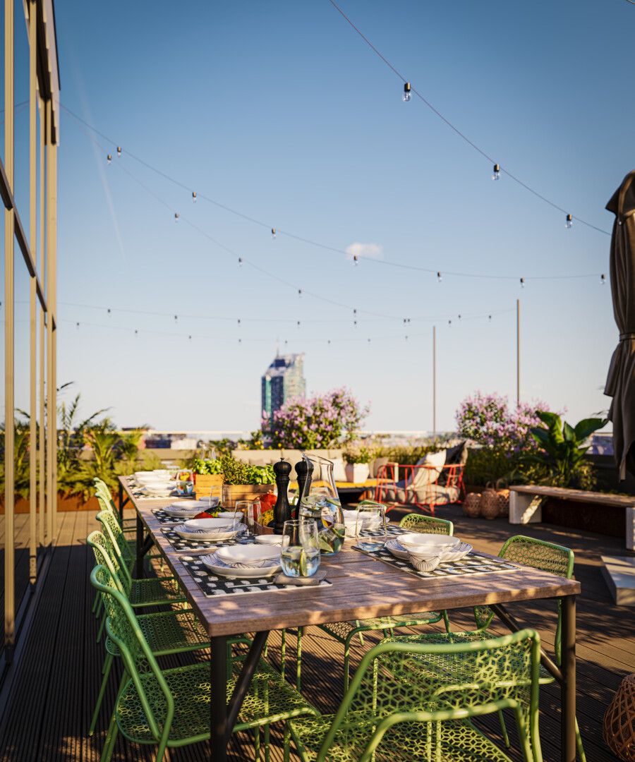 Uteservering med dukat träbord, gröna stolar och utsikt över stadens skyline, omgiven av växter och ljusslingor
