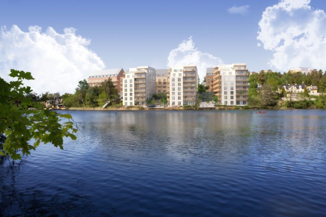 Vy över en sjö med moderna bostadshus och grönområden i bakgrunden under en klar blå himmel
