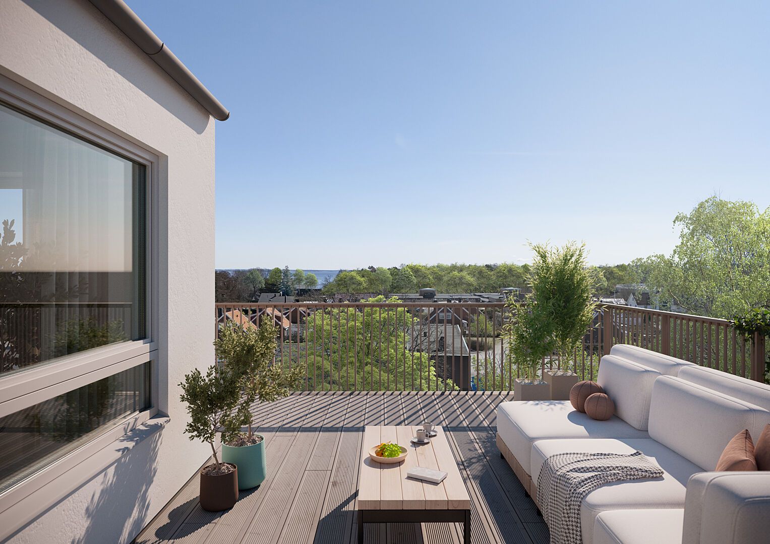 Terrass med trämöbler och växter, utsikt över hustak, träd och hav under klarblå himmel