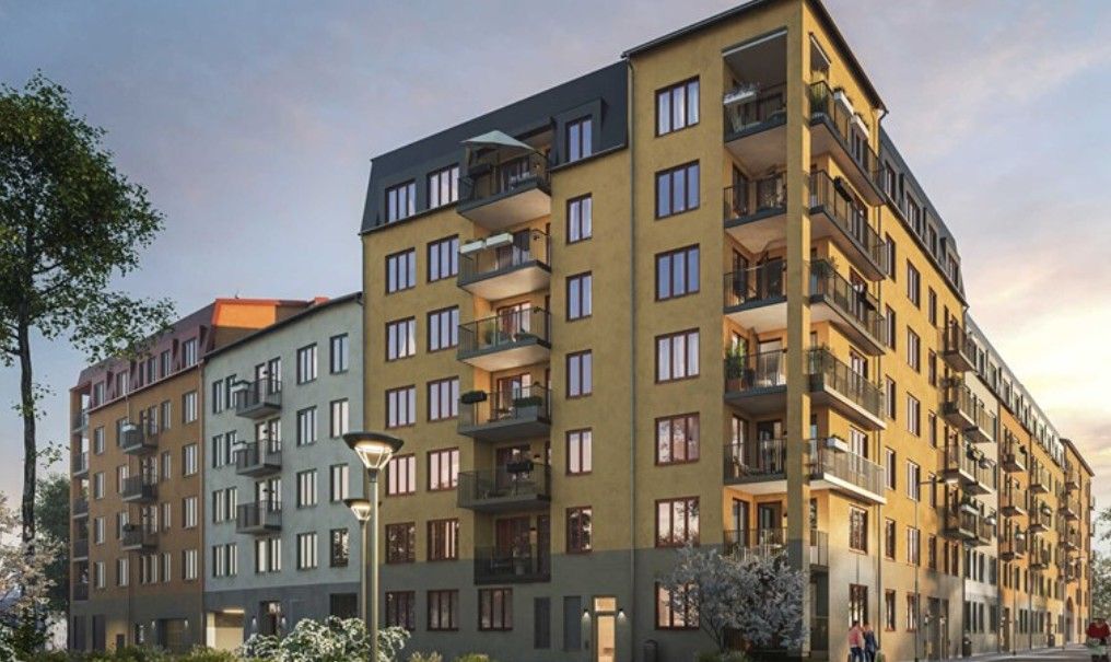 Flerbostadshus med gul och grå fasad, flera balkonger och omgivande träd i ett stadsområde under solnedgång