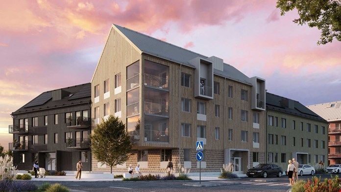 Flervåningshus med modern design, träfasad och stora fönster, beläget vid en gata med parkerade bilar och promenadstråk under en färgglad solnedgång