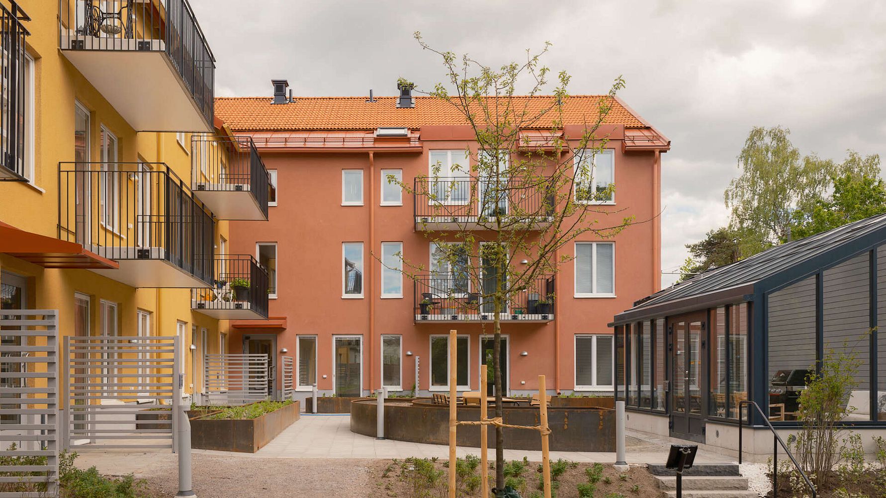 Flerbostadshus med färgglada fasader och balkonger, omgivna av en gård med nyplanterade träd och gångvägar
