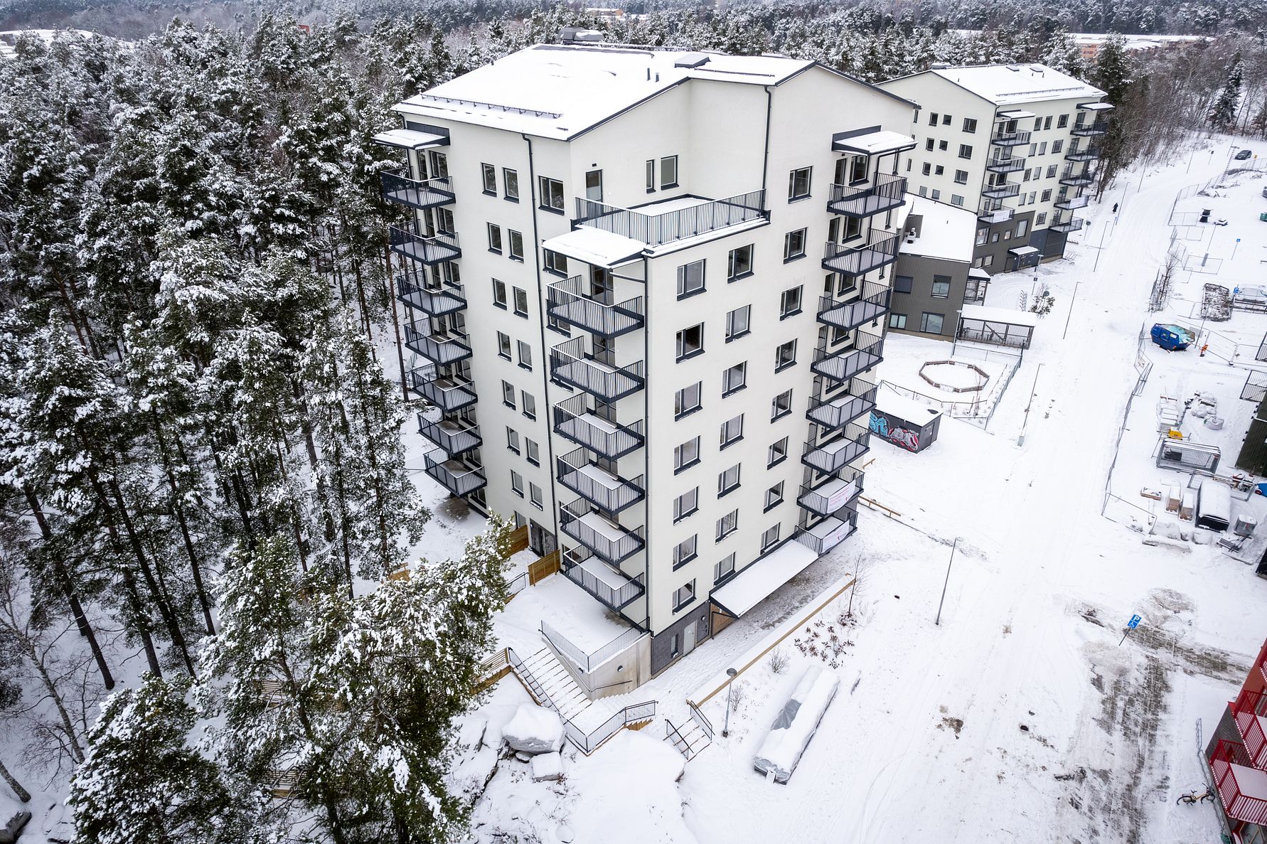 Lägenhetskomplex i flera våningar omgivet av snötäckta träd och byggmaterial under vintertid