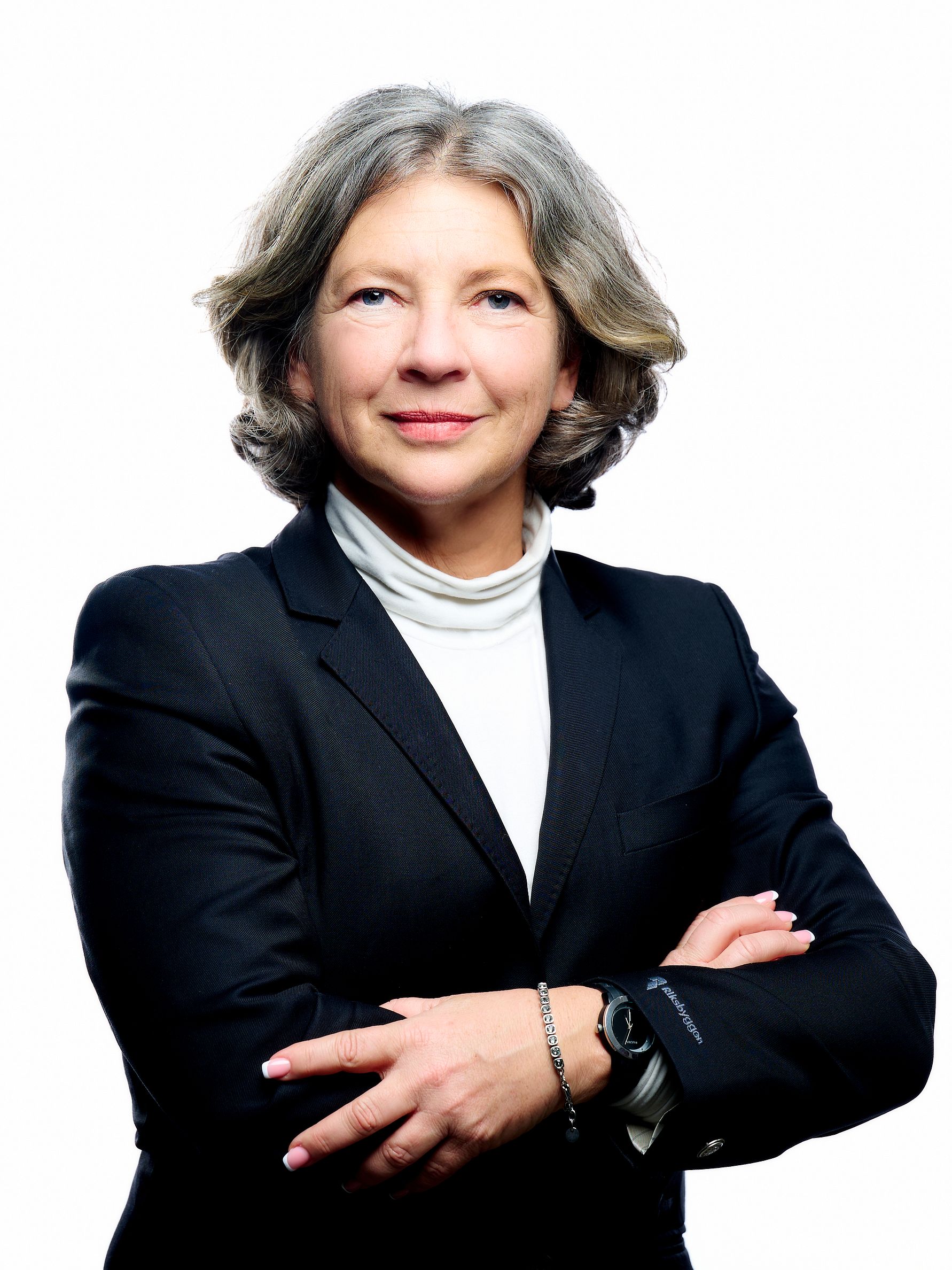 En person i kostym med korslagda armar, vit skjorta och armbandsur, framför en vit bakgrund