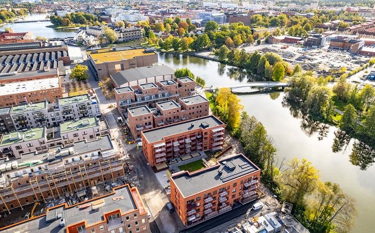Flygfoto över ett bostadsområde med flera moderna byggnader, omgivna av grönområden och en vattenkanal i en urban miljö