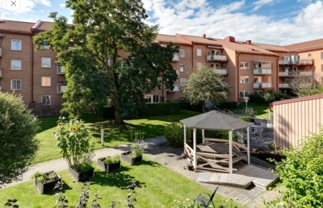 Flerbostadshus i tegel med gröna träd och en trädgård utrustad med en paviljong och odlingslådor