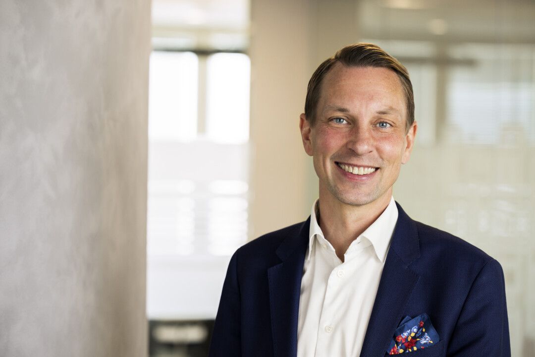 Man i kostym med en mörkblå blazer, vit skjorta och en färgglad näsduk i bröstfickan, stående i en ljus kontorsmiljö