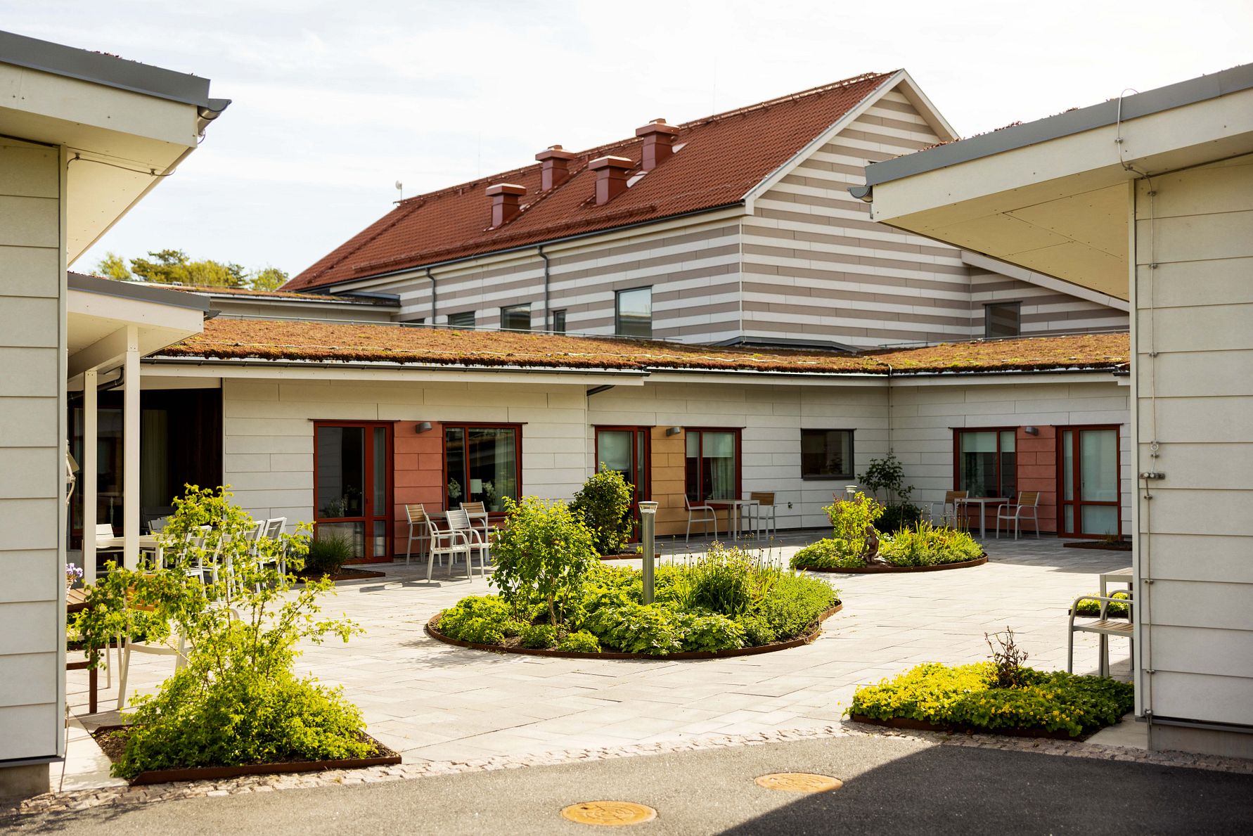 Innergård med grönska, utemöbler och moderna byggnader med röda tak och träfasader