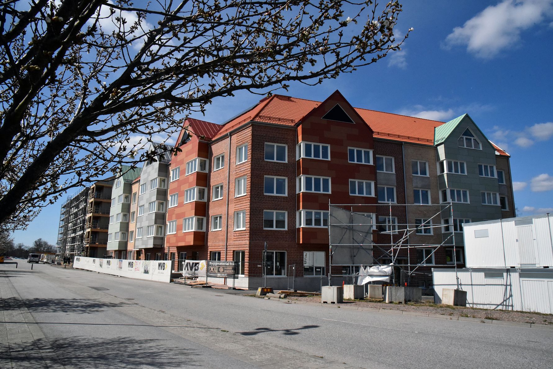 Flerbostadshus under byggnation med tegel- och färgglad fasad, omgivna av byggarbetsplats och klarblå himmel