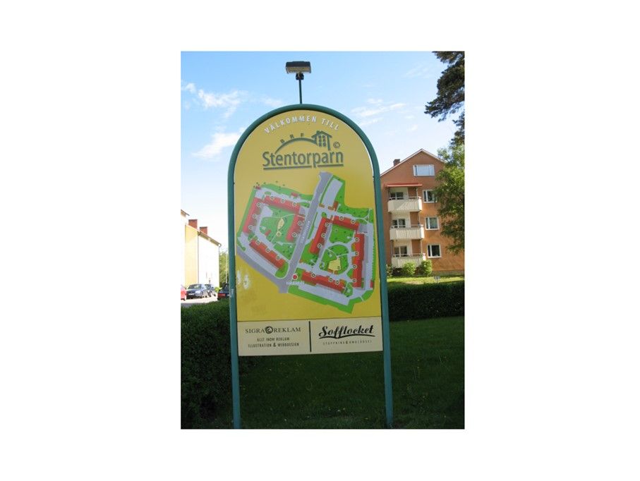 Skylt med texten "Stentorparn" och en karta över området, omgiven av flerfamiljshus och grönska under en klarblå himmel