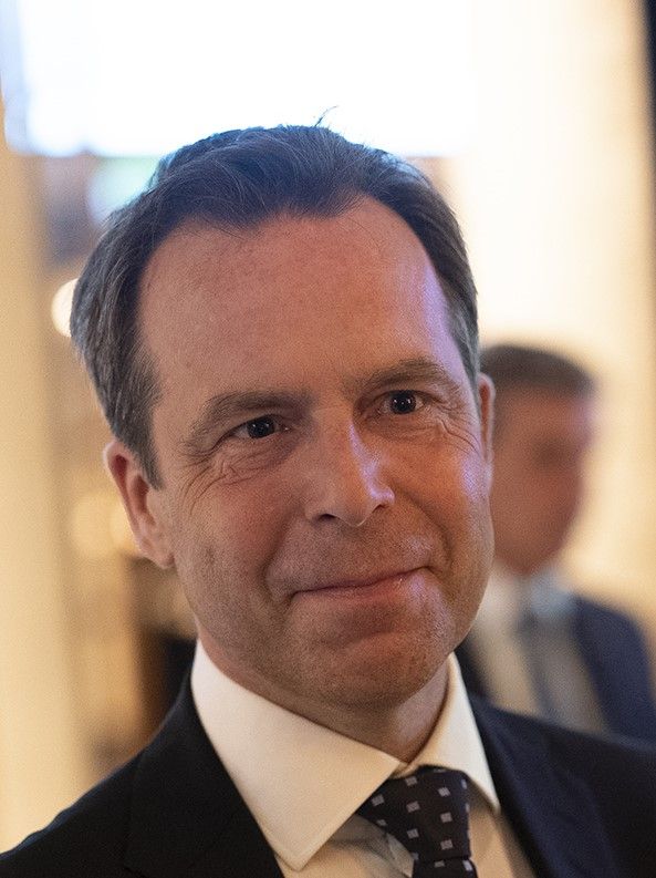 Man i kostym och slips står inomhus med suddig bakgrund