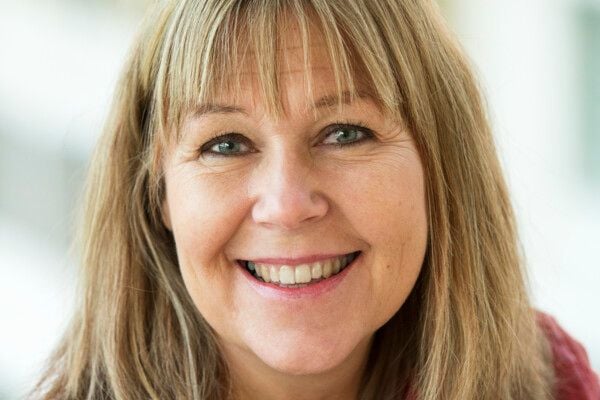 En person med ljust brunt hår som faller ner över axlarna, med en suddig bakgrund i ljusa färger