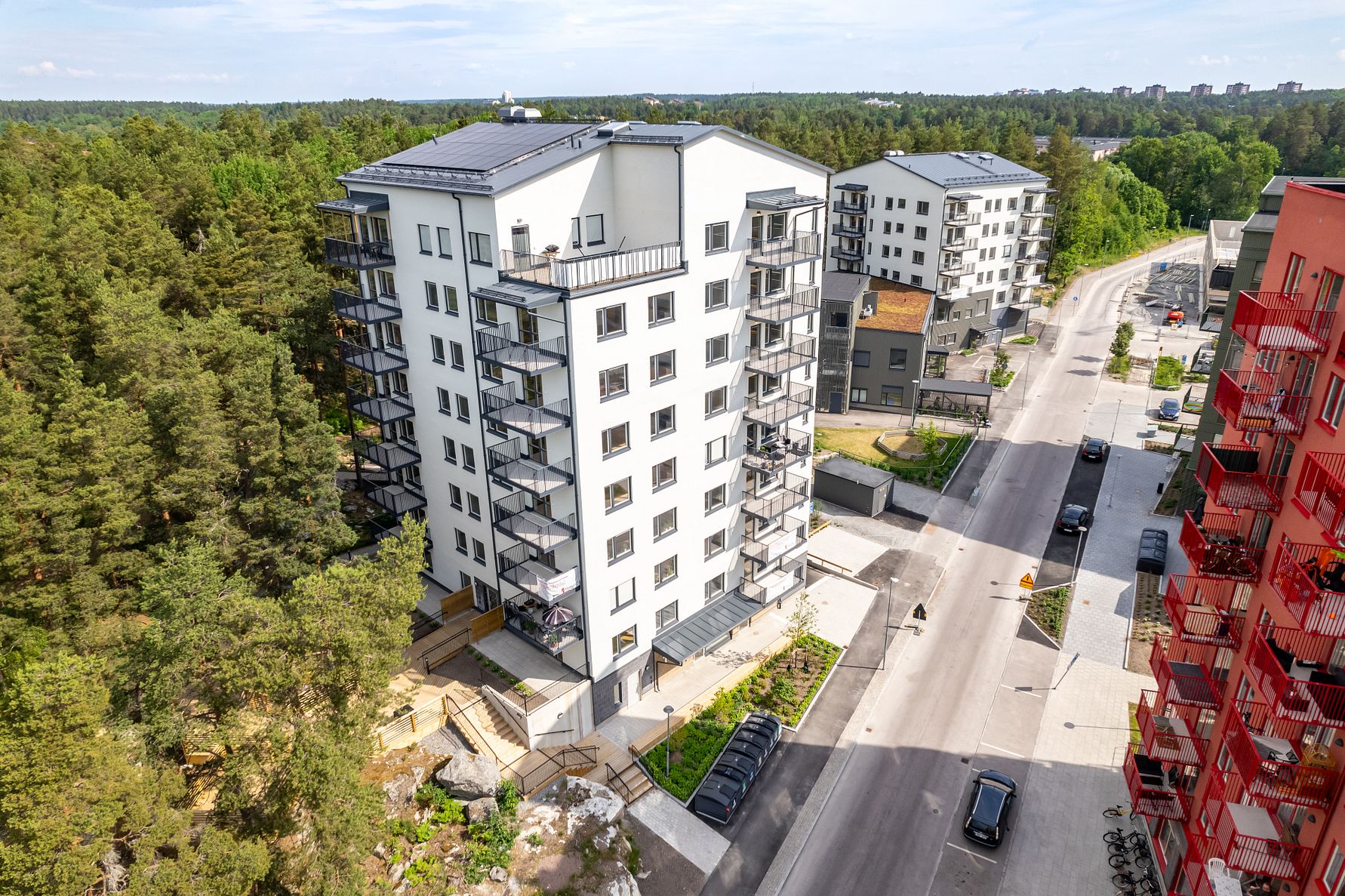 Flerfamiljshus med moderna fasader och balkonger, beläget vid en gata omgiven av grönska och andra byggnader
