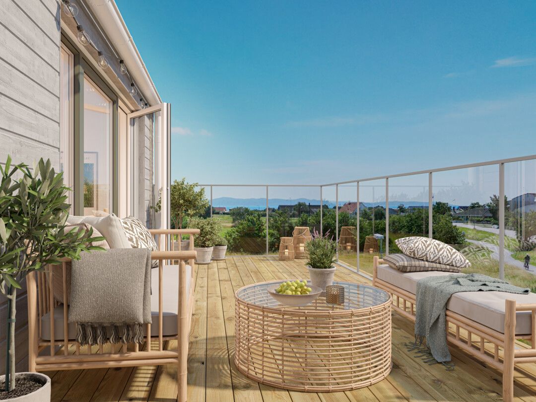 Rymlig terrass med trämöbler, kuddar och filtar, dekorerad med växter, med utsikt över grönska och blå himmel