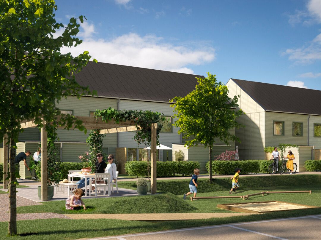 Nybyggda radhus med fasader i ljus färg omgivna av grönska, lekande barn, och vuxna som umgås vid ett bord under en pergola