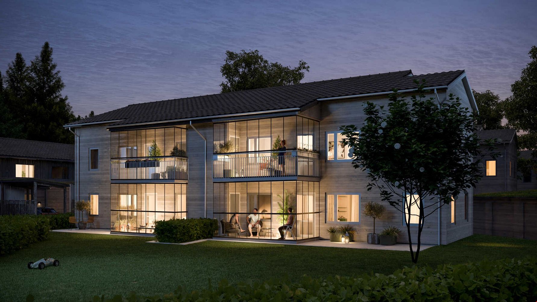 Tvåvåningshus med modern design, stora glaspartier och balkonger, omgiven av en gräsmatta och träd vid skymning