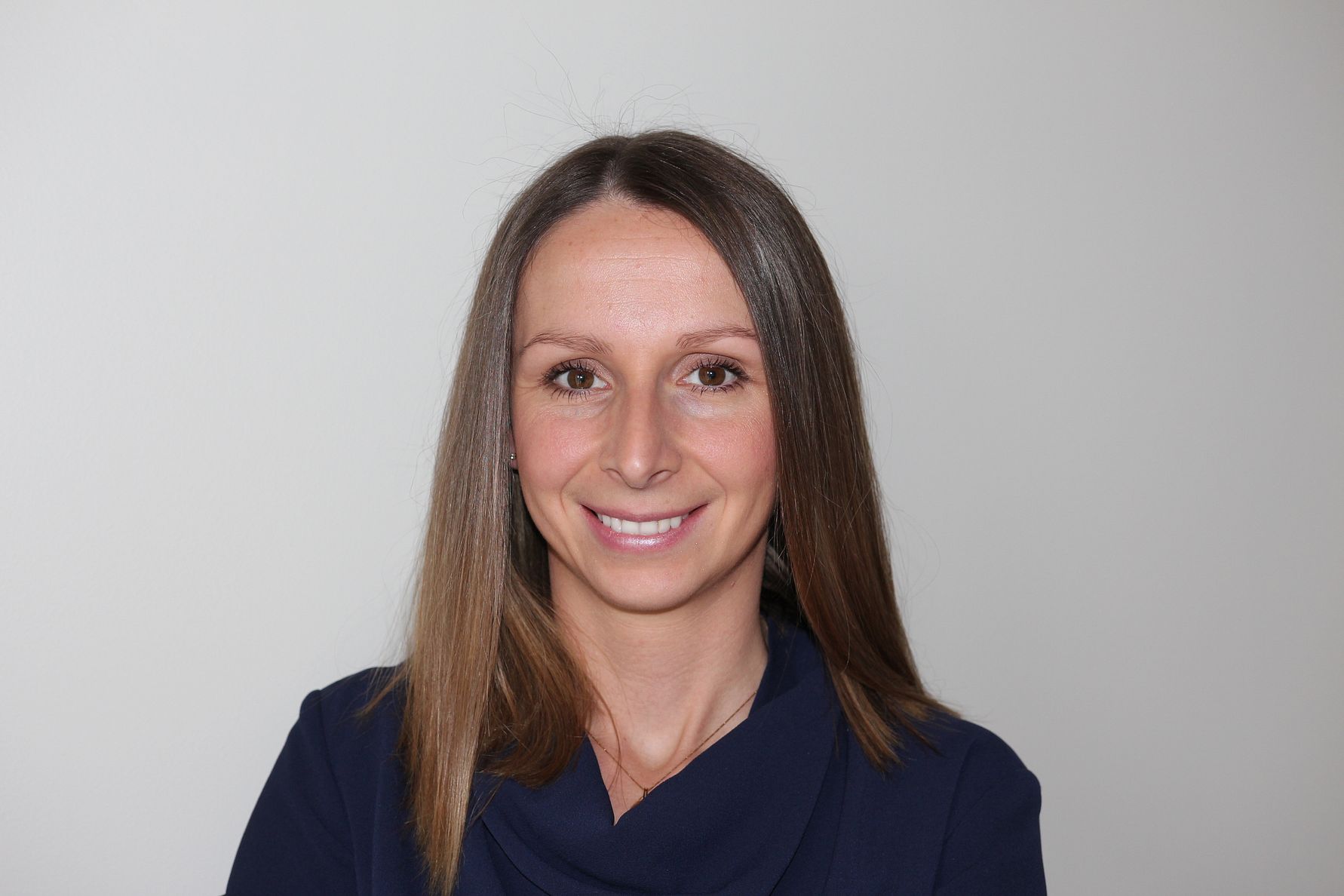 Kvinna med axellångt brunt hår och mörkblå topp framför en ljus, enfärgad bakgrund