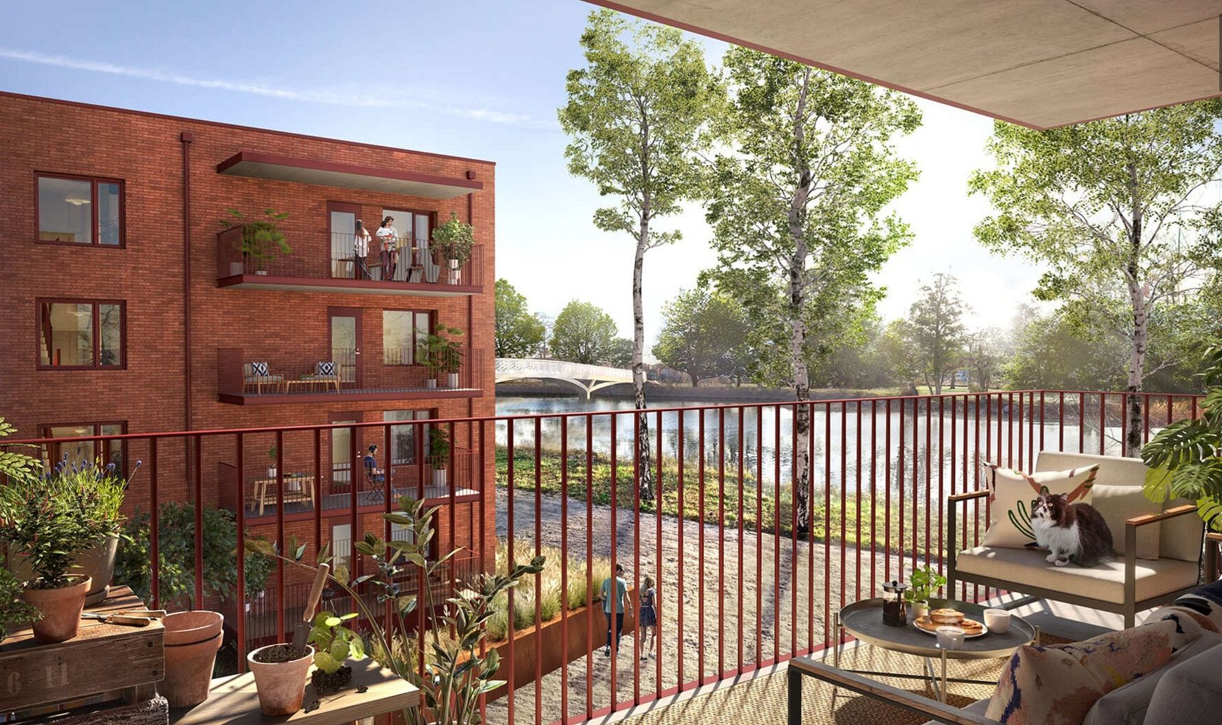 Balkong med utsikt över en innergård med röda tegelbyggnader, grönskande träd och en å i bakgrunden