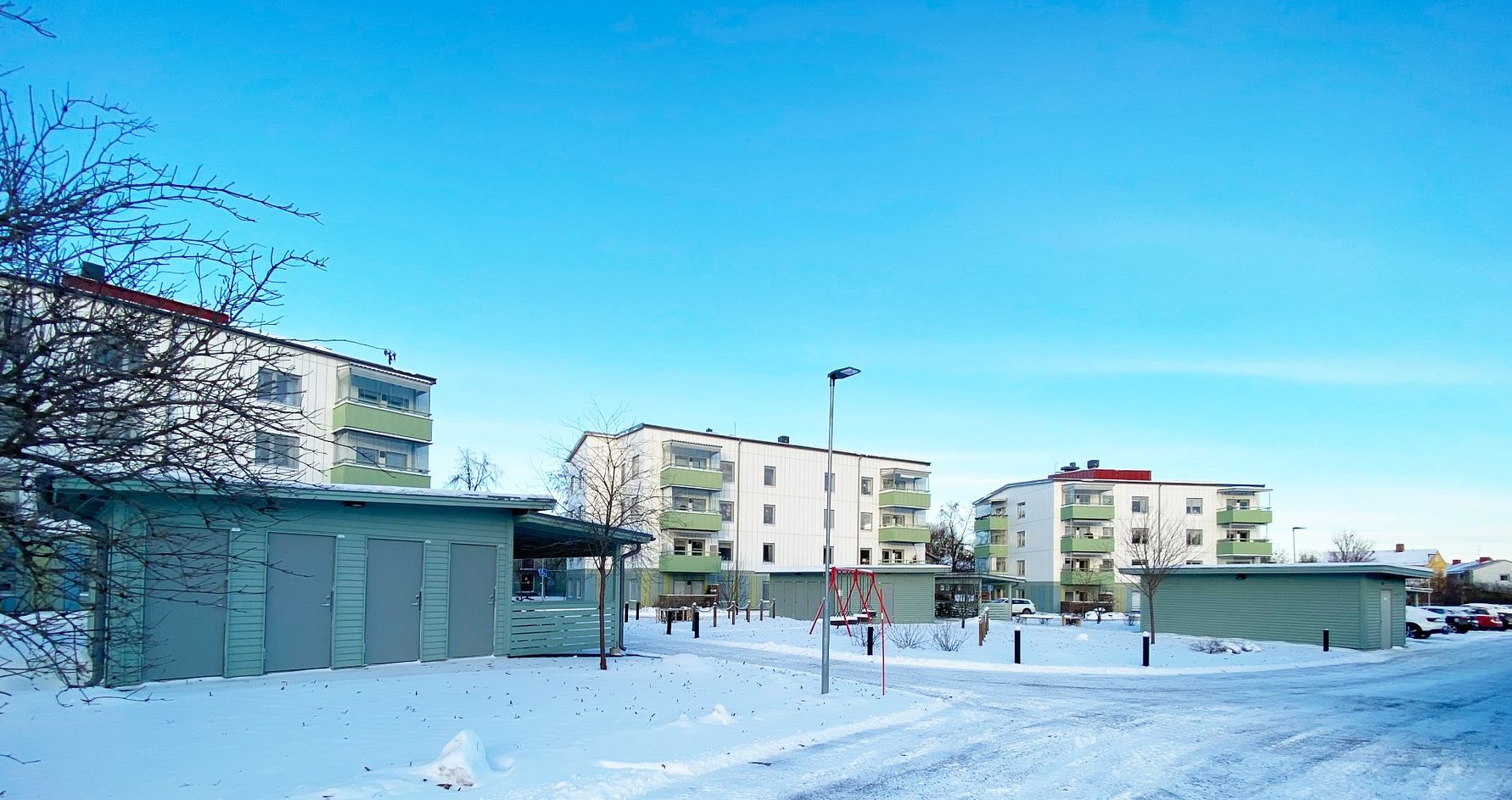 Flerbostadshus och garagebyggnader omgivna av snö under en klar blå himmel