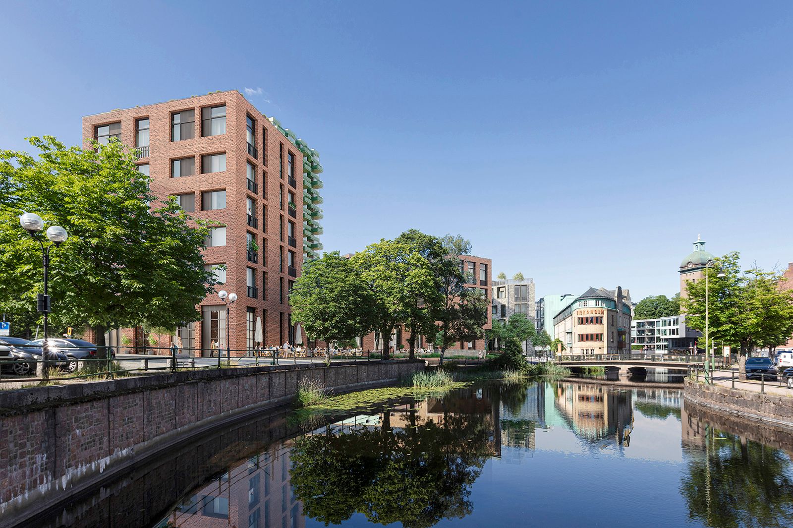 Flodkant med moderna byggnader i tegel, träd och blå himmel i en stadsbild