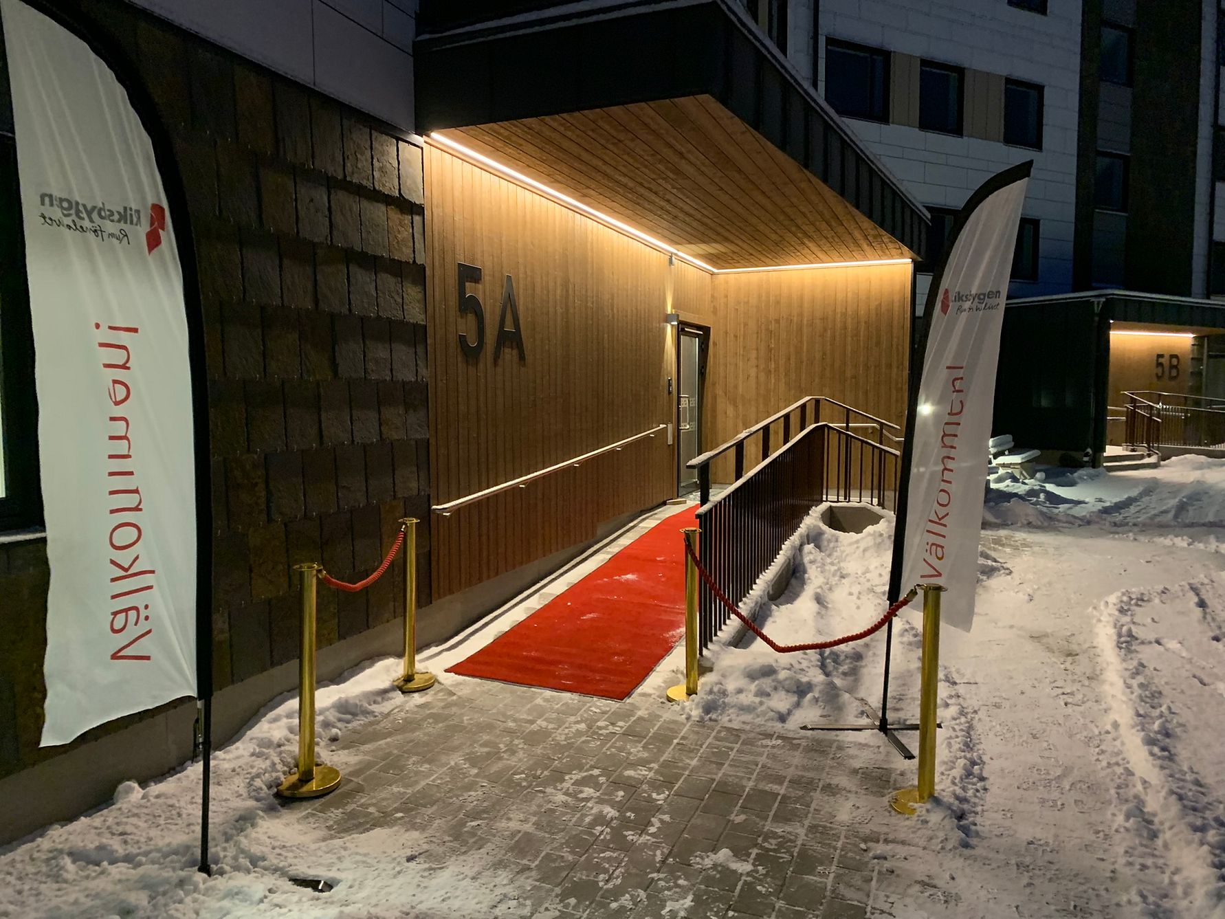 Entré till en byggnad med röda mattan, snö på marken och två flaggor som säger "Välkommen