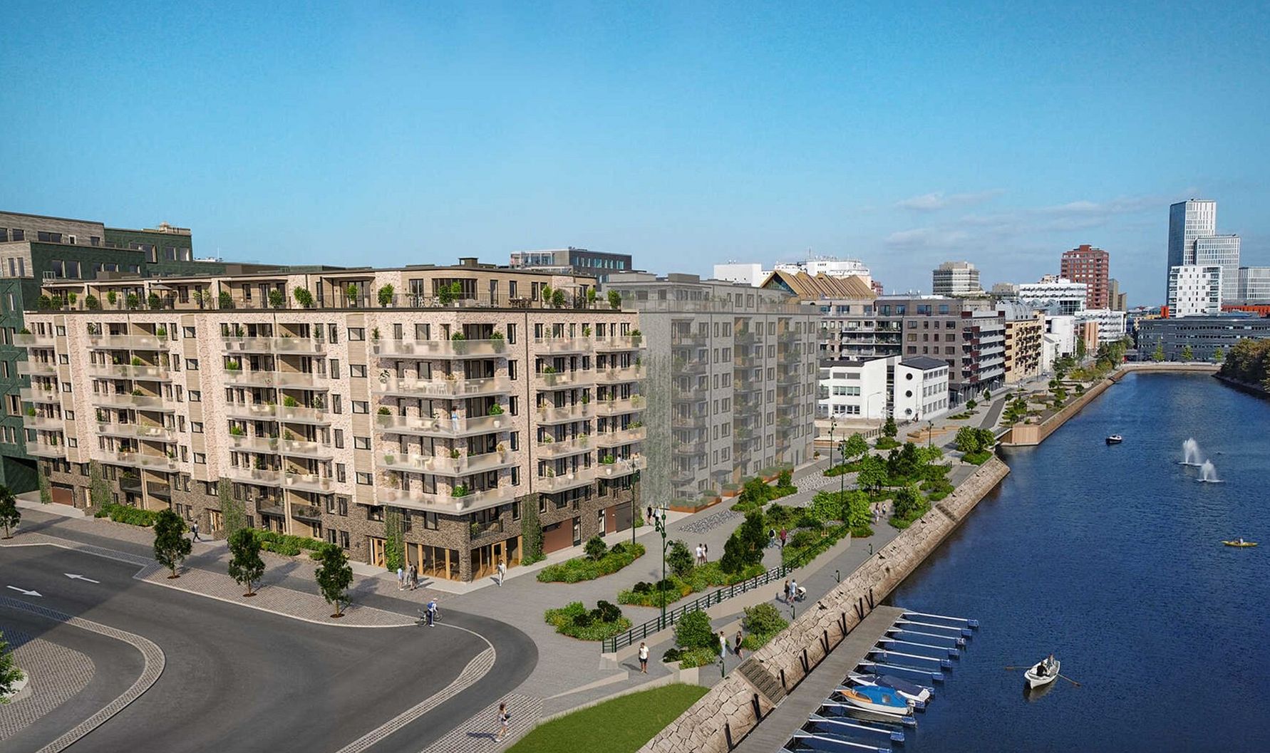 Vy över en modern stadsdel med flerbostadshus, gröna områden och en kanal med småbåtar, under en klar blå himmel