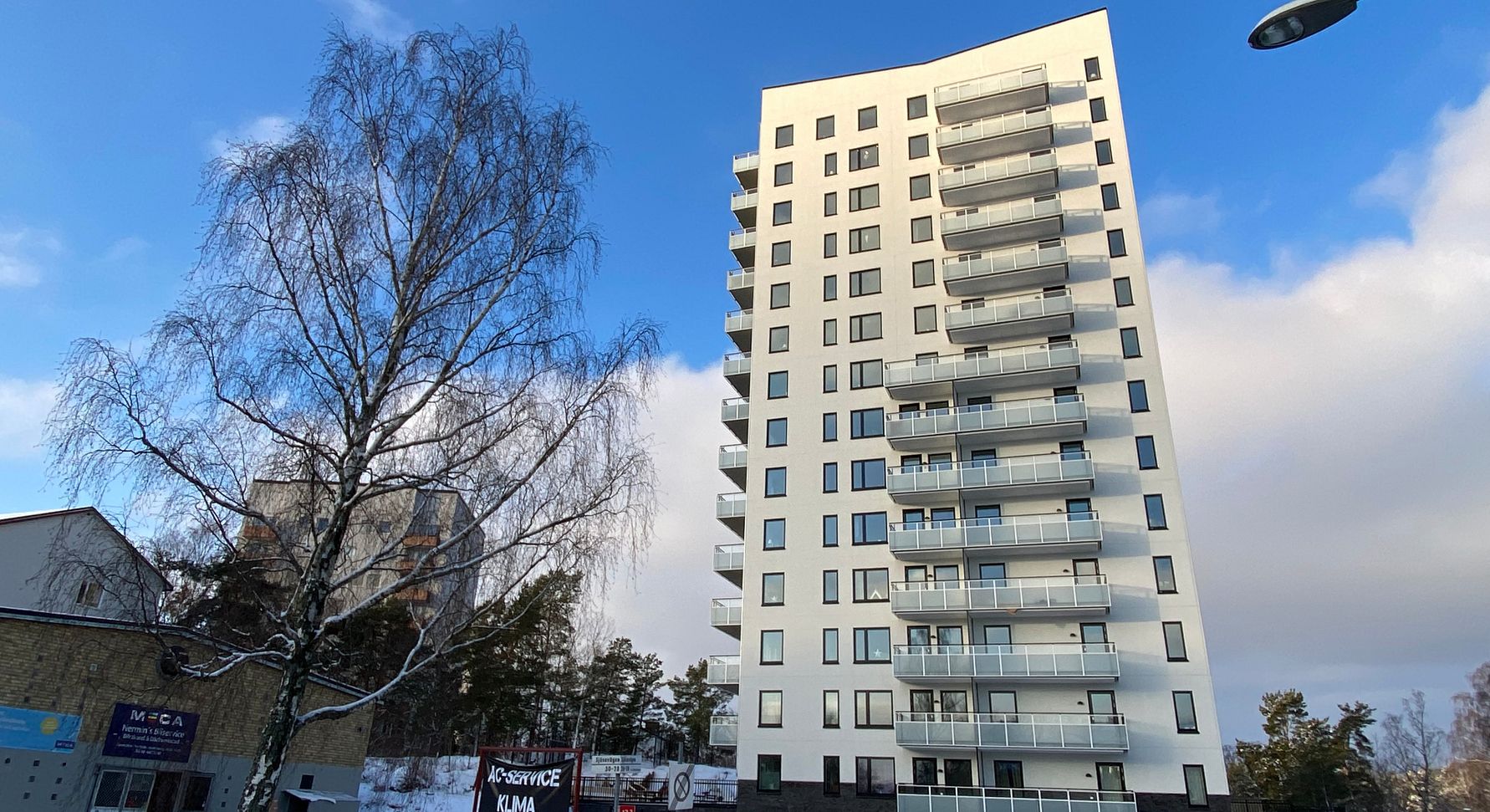 Höghus med flera våningar och balkonger, omgivna av träd, en byggnad och en klar blå himmel