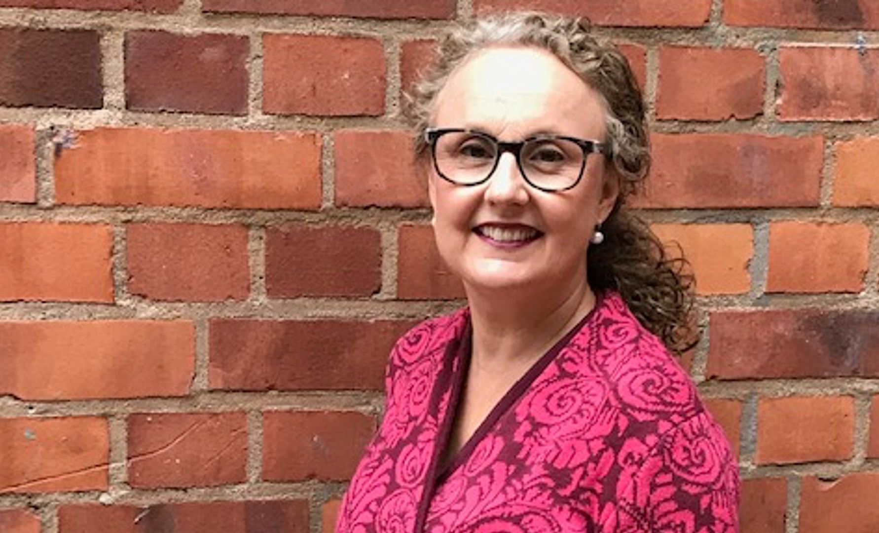 Kvinna i rosa mönstrad tröja står framför en röd tegelvägg