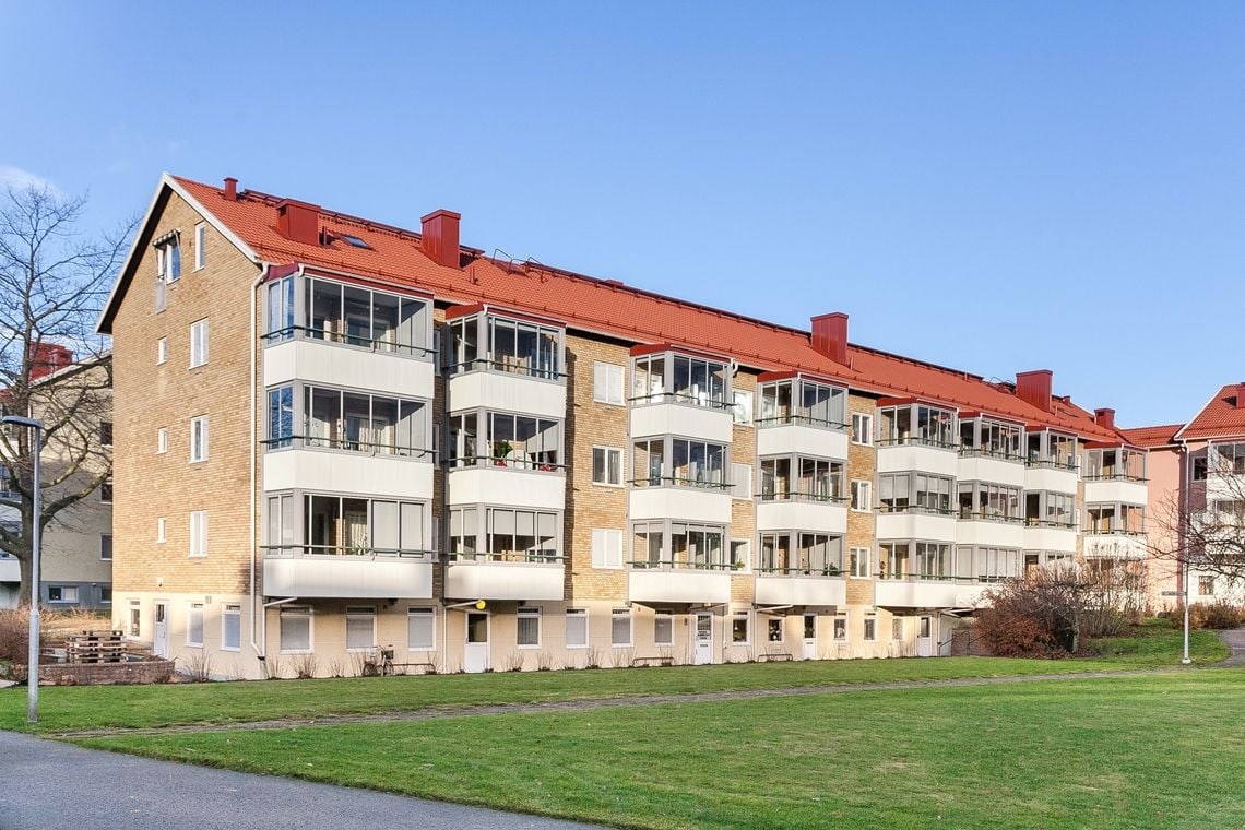 Flerbostadshus i tegel med röda tak, flera balkonger och grönområde i förgrunden under en klarblå himmel