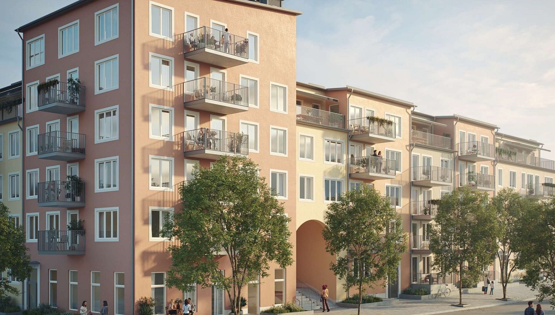 Lägenhetsbyggnad med flera våningar, balkonger och pastellfärgad fasad, omgiven av träd och människor på gångvägen