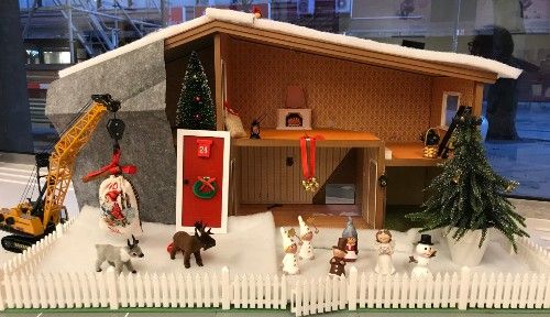 Miniatyrjulscen med ett hus, grävmaskin, snö, juldekorationer och figurer som djur, snögubbe och människor omgivet av ett vitt staket