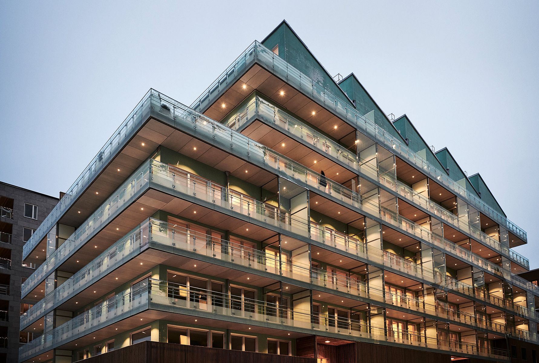 Modern flerfamiljshus med glasbalkonger och triangulära tak, fotograferat under kvällsbelysning