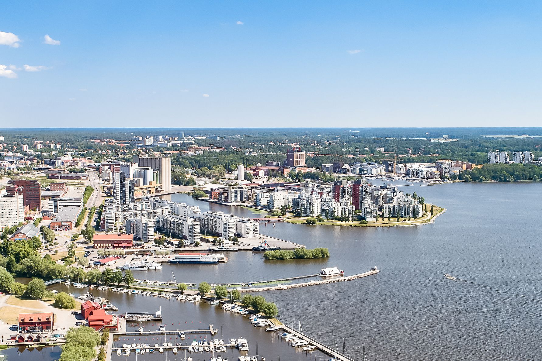 Flygbild av Västerås med Mälaren och båthamnar i förgrunden samt stadsbebyggelse och grönområden i bakgrunden
