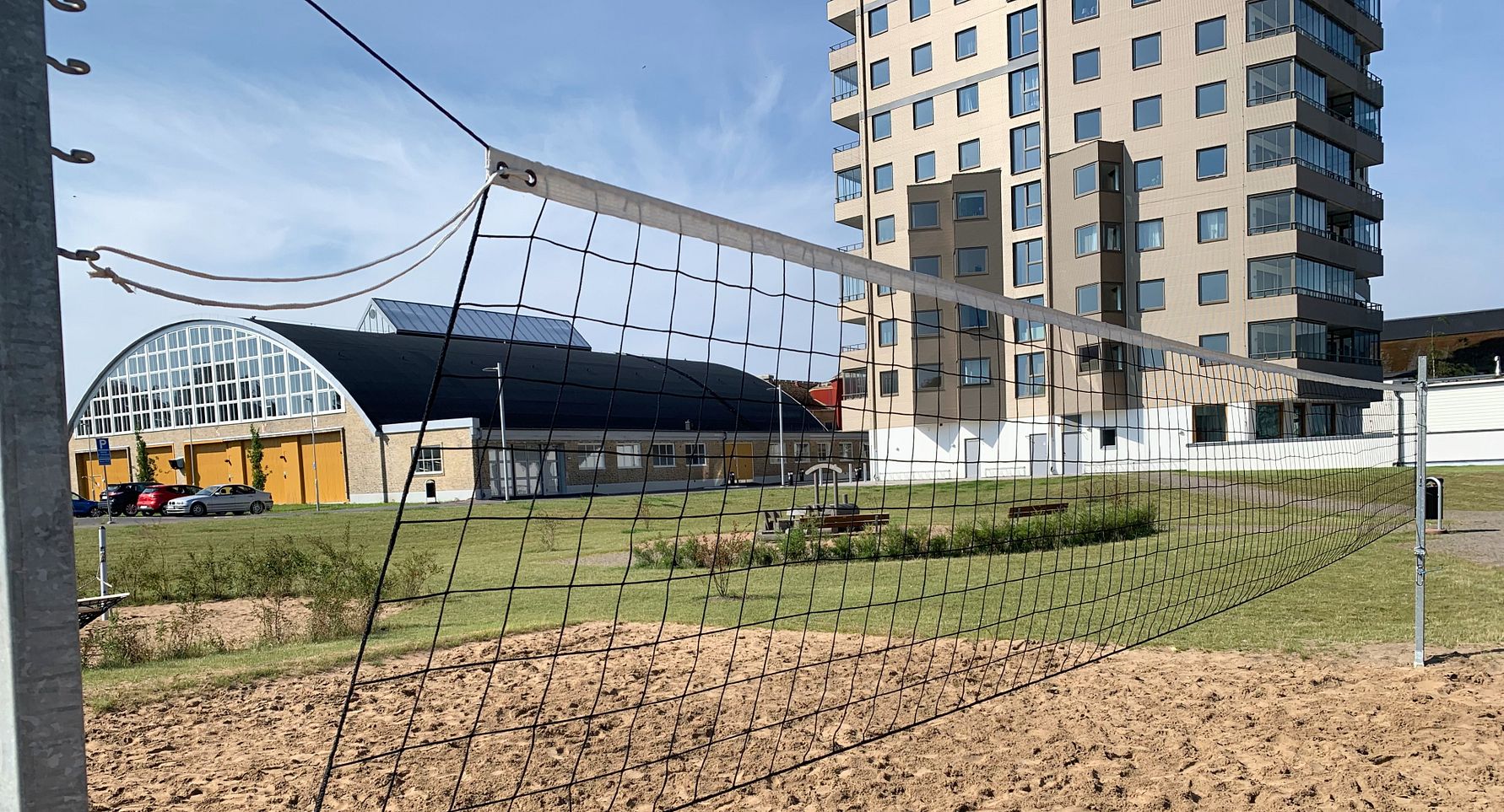Sandvolleybollplan framför en gräsyta, med moderna byggnader och en flerbostadshus i bakgrunden