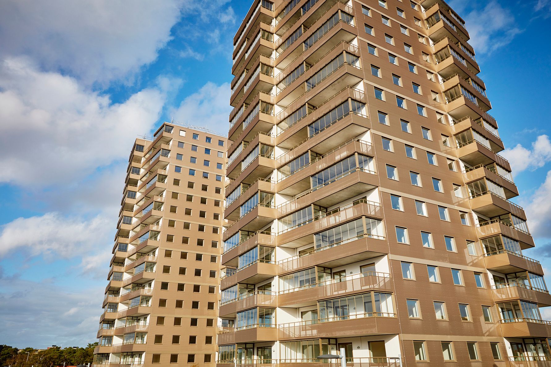 Två moderna lägenhetskomplex med balkonger, sett mot en blå himmel med moln