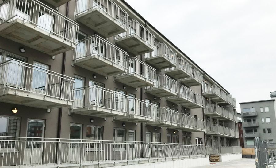 Flerfamiljshus med flera våningar och balkonger i metall, med grå fasad och omgivande stadsbyggnader