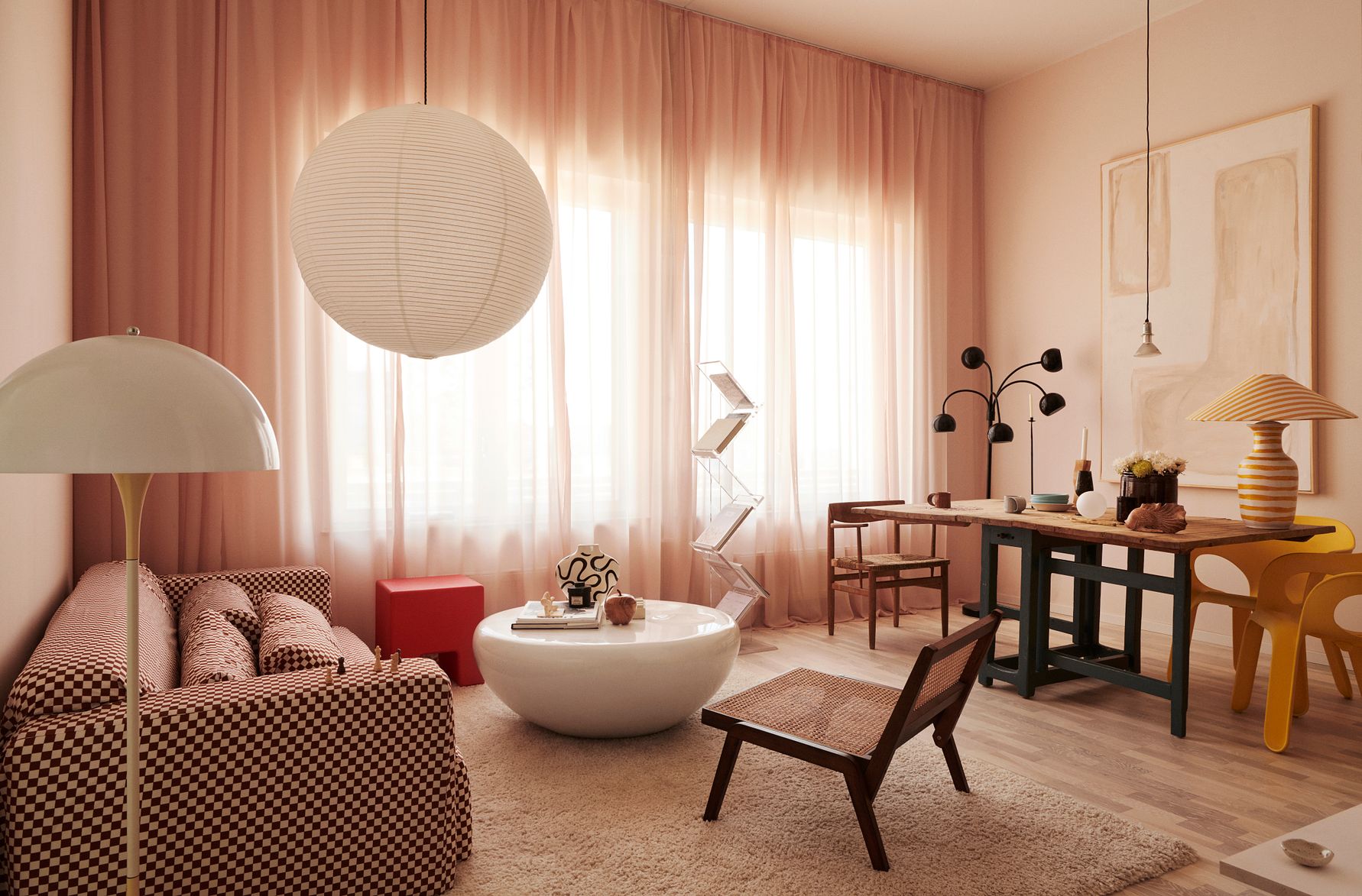 Ljus vardagsrum med rosa gardiner, mönstrad soffa, rund vit soffbord, modern belysning och en matplats med färgglada stolar