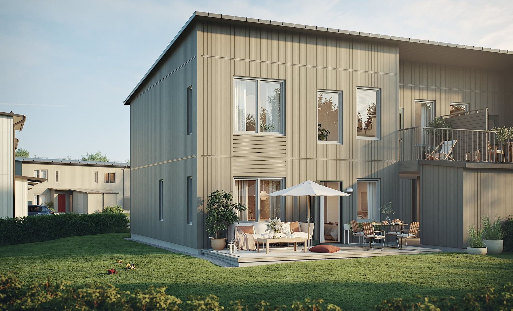 Modern tvåvåningshus med träfasad, stora fönster och en terrass med utemöbler och solparasoll, omgiven av gräsmatta och buskar