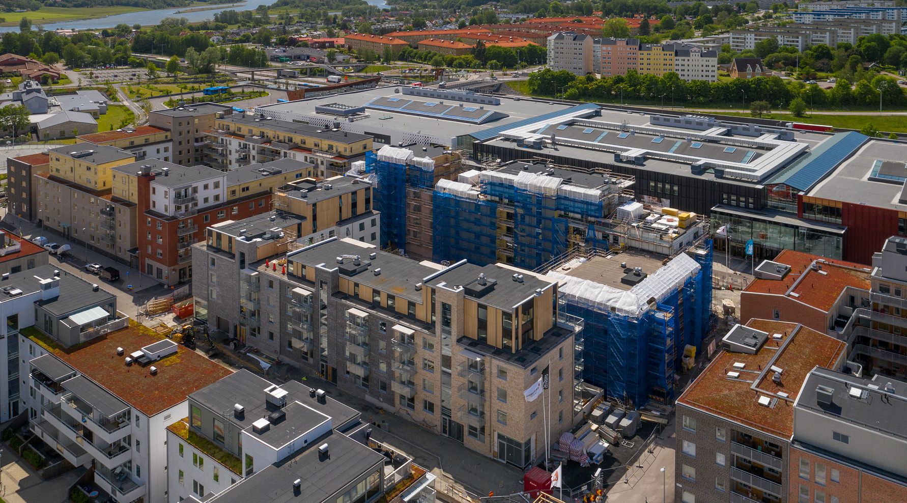 Flygbild över ett bostadsområde med flerfamiljshus, byggnadsarbetsplatser och ett köpcentrum i bakgrunden