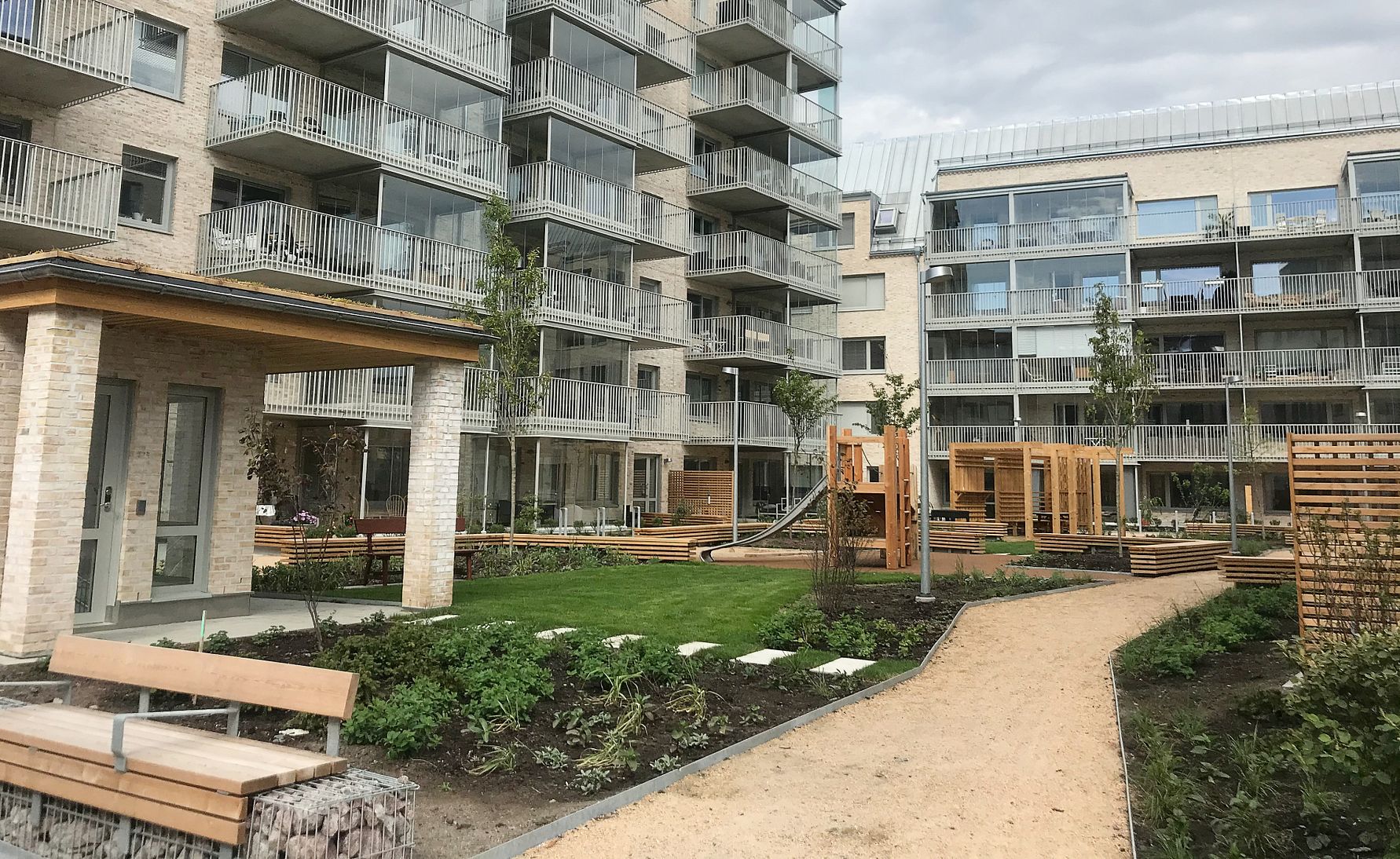 Modern bostadsområde med flerfamiljshus, grönområden och gångvägar. Lägenhetsbyggnader med balkonger omger en välskött innergård
