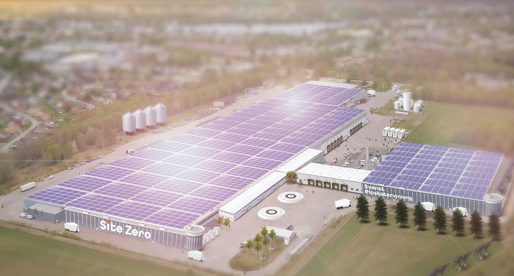 Flygvy över Site Zero, en anläggning med stora solpaneler på taket, omgiven av grönområden och byggnader